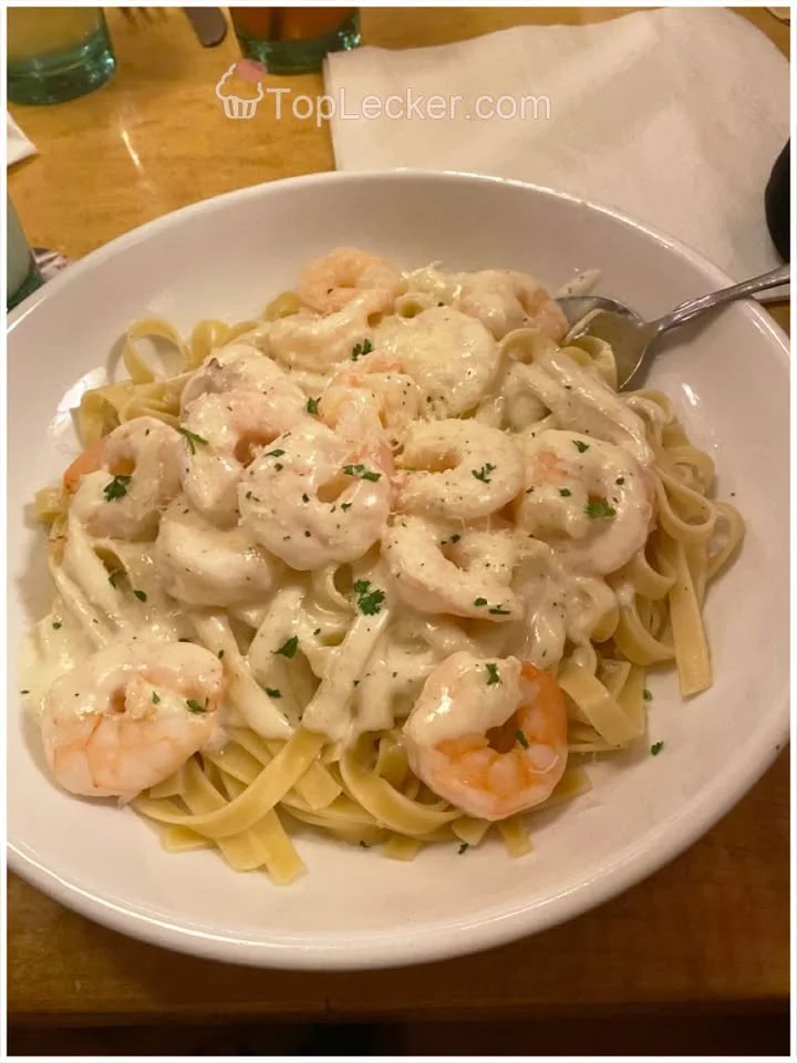 Tagliatelle mit Garnelen in weißer Weincremesoße auf einem Teller.