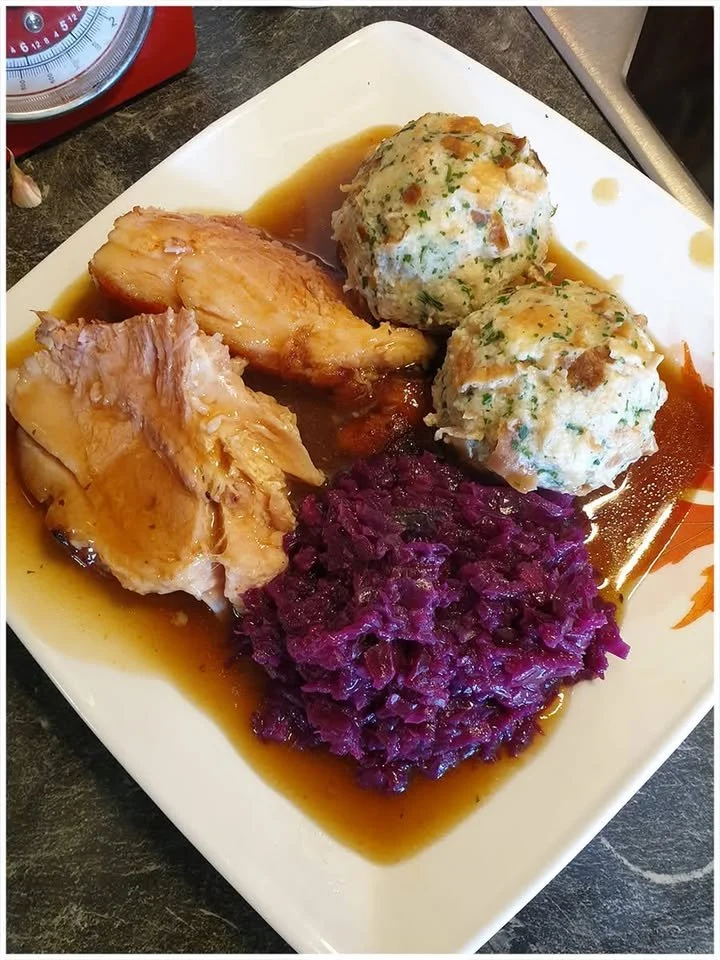 Schweinebraten mit Sauce, Rotkohl und Klößen auf einem Teller serviert