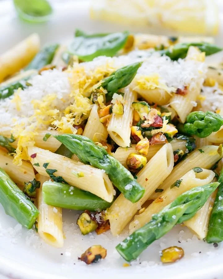 Pasta mit grünem Spargel auf einem weißen Teller garniert mit Parmesan.
