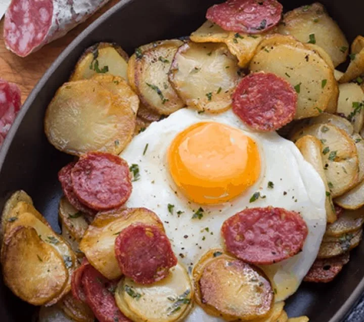 Bratkartoffeln mit Wurst und Spiegelei auf einem Teller serviert
